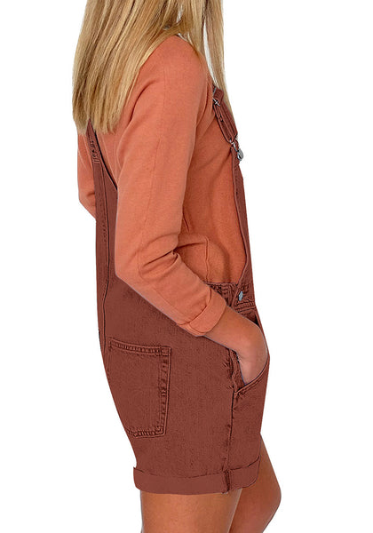 Side view of model wearing rust red rolled hem shorts denim bib overall
