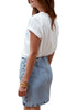 Angled back view of a posing model wearing light blue acid wash tulip ruched denim mini skirt