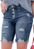 Angled shot of model wearing deep blue frayed hem ripped button-up denim bermuda shorts