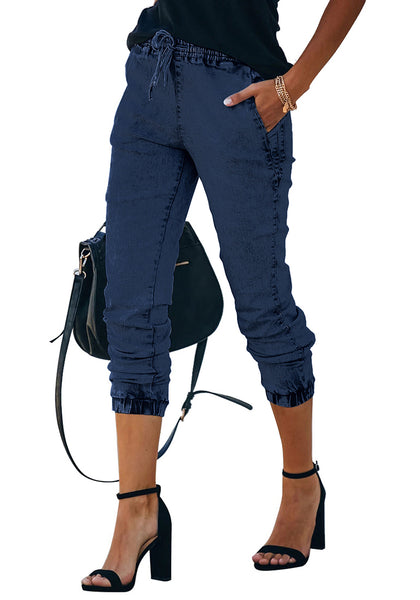 Closeup view of model wearing deep blue elastic-waist welt pockets denim jogger pants