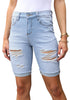 Front view of model wearing light blue plus size mid-waist ripped denim bermuda shorts.