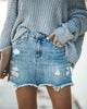 Front view of model wearing light blue frayed raw hem distressed denim mini skirt