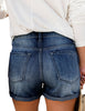 Back view of model wearing dark blue triple button faded distressed denim shorts