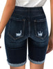 Back view of model wearing dark blue mid-waist raw hem distressed denim bermuda shorts