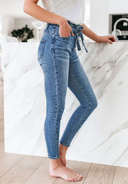 Side view of model wearing blue high-waist acid wash belted denim skinny jeans