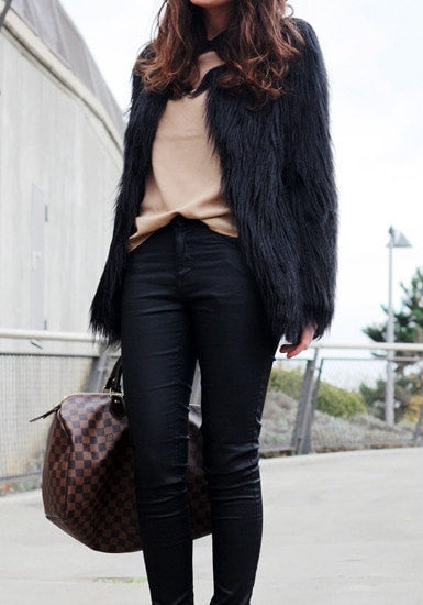 Angled view of model in black faux fur coat with bag